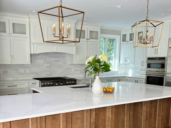 Modern white kitchen with brass chandeliers and large marble island