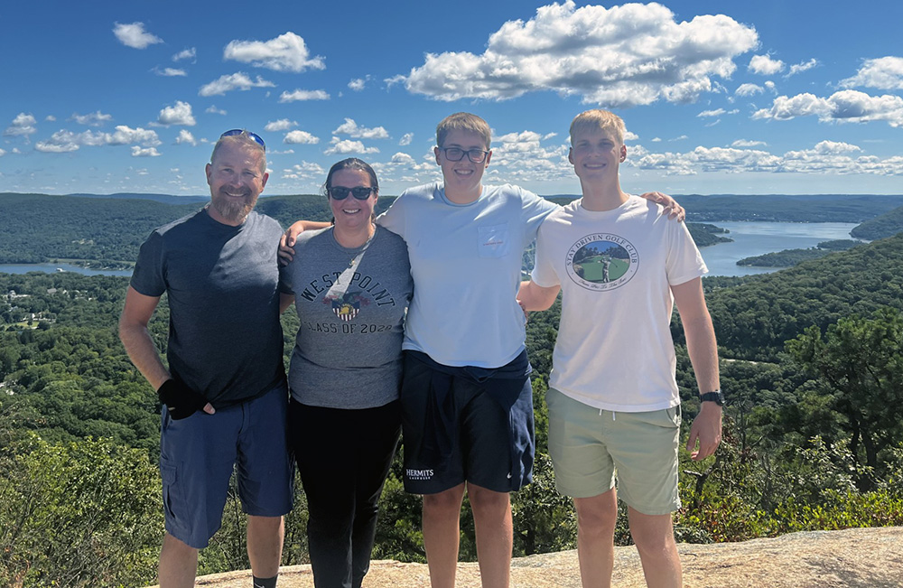 Four people pose overlooking a lake and forested hills.